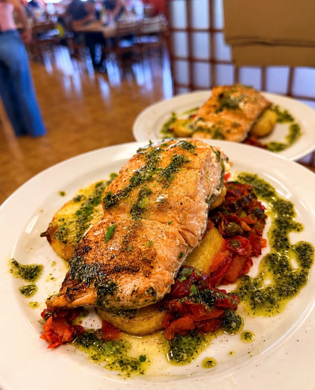 Salmón a la plancha con salsa verde y patatas, con el comedor al fondo